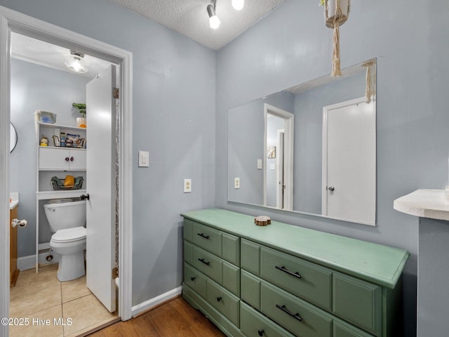 bathroom with toilet, vanity, a textured ceiling, and baseboards