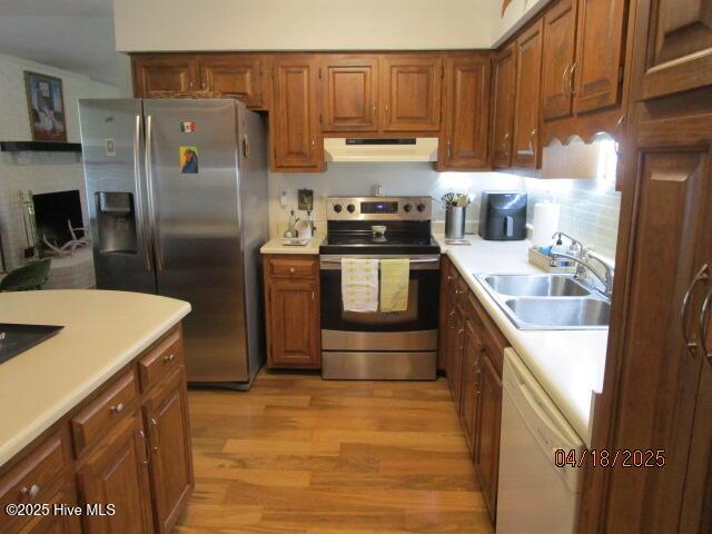kitchen featuring stainless steel appliances, extractor fan, a sink, light wood-style floors, and brown cabinetry