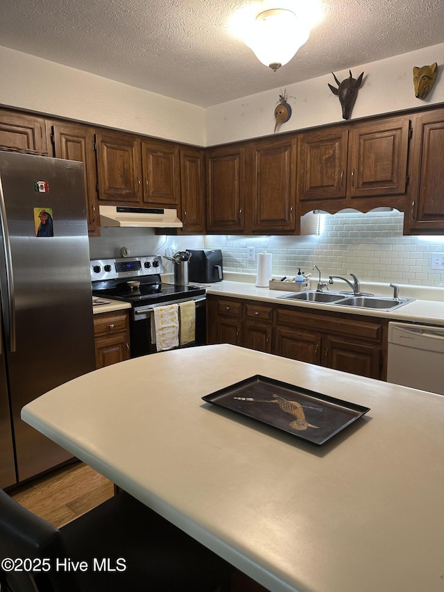 kitchen featuring appliances with stainless steel finishes, a sink, light countertops, and under cabinet range hood