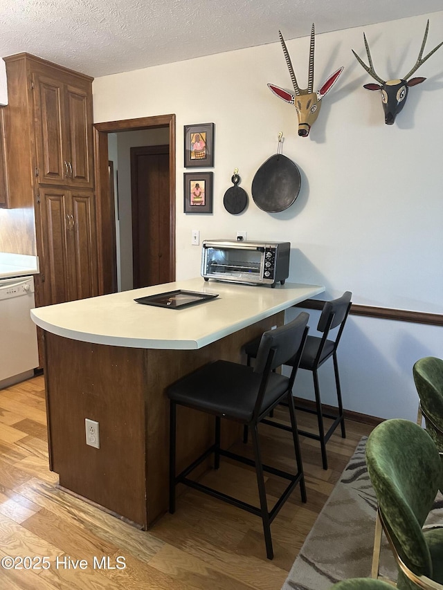 kitchen with white dishwasher, light wood-type flooring, a kitchen bar, light countertops, and a textured ceiling