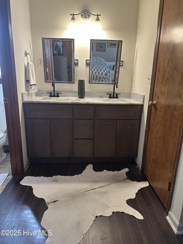bathroom featuring wood finished floors, double vanity, toilet, and baseboards