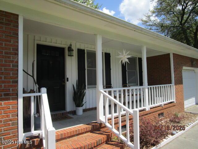 view of exterior entry with a porch, brick siding, and crawl space