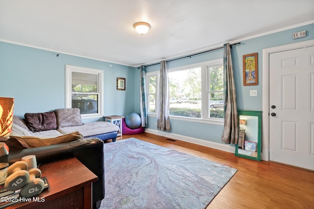 living room featuring wood finished floors, visible vents, baseboards, and ornamental molding