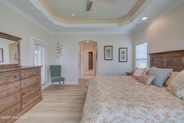 bedroom featuring crown molding, arched walkways, a tray ceiling, light wood finished floors, and visible vents
