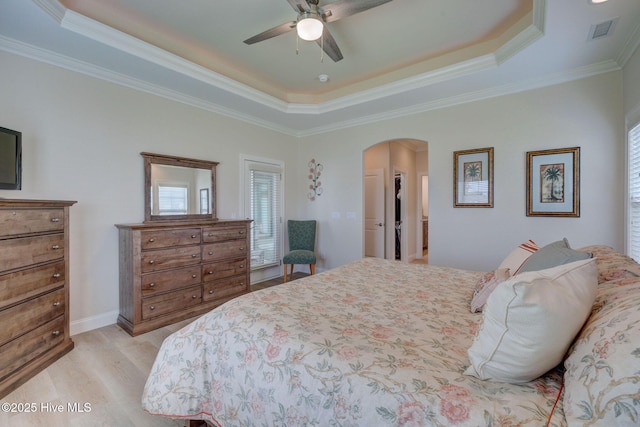 bedroom featuring crown molding, arched walkways, a tray ceiling, light wood finished floors, and visible vents
