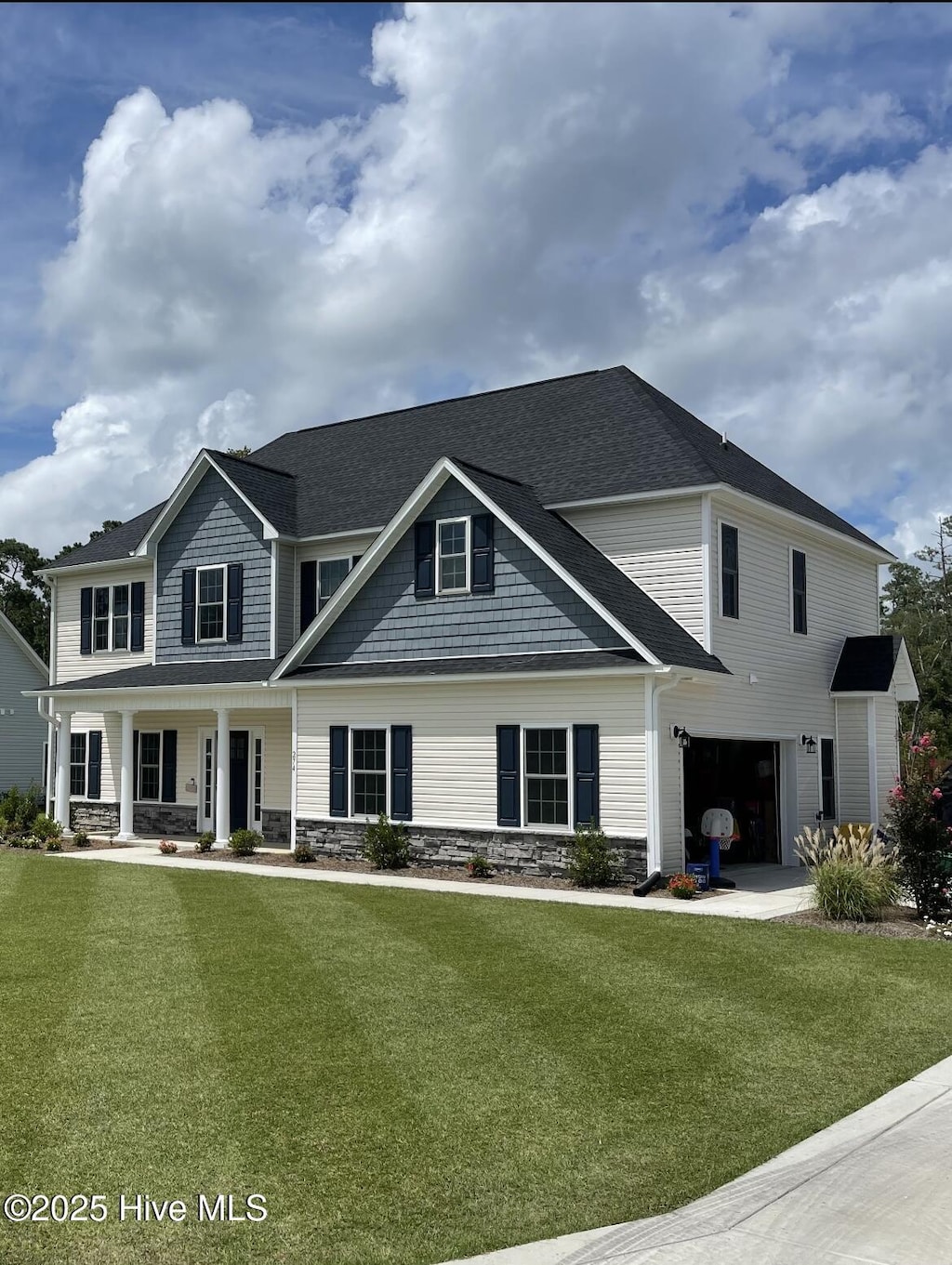 view of front of property featuring a porch, a front lawn, an attached garage, a shingled roof, and stone siding