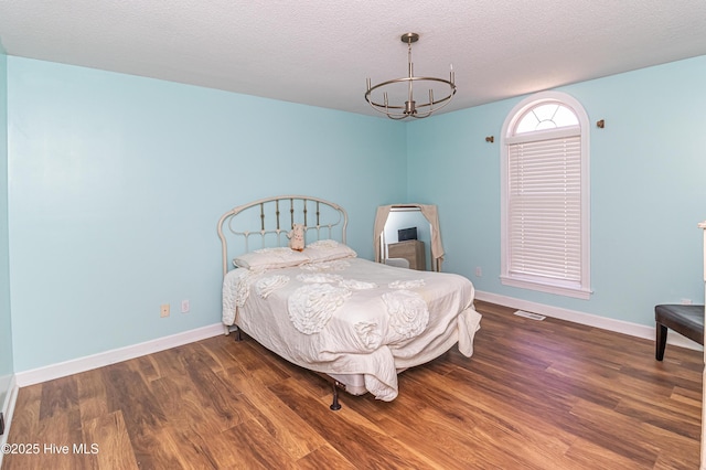bedroom featuring visible vents, wood finished floors, baseboards, a textured ceiling, and a notable chandelier