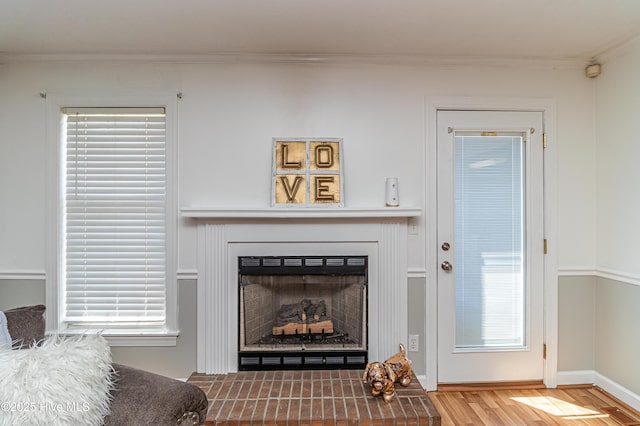 living room featuring crown molding, baseboards, a fireplace with raised hearth, and wood finished floors