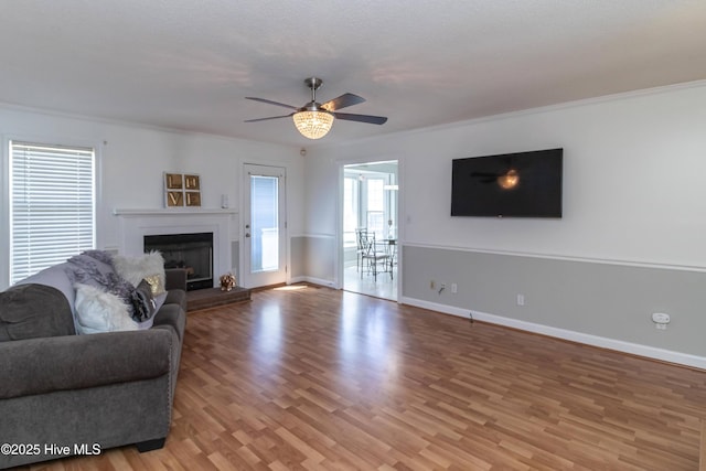 living area featuring ornamental molding, light wood-style floors, baseboards, a fireplace with raised hearth, and a ceiling fan