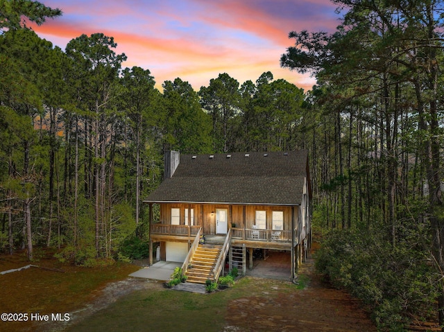 121 Pinewood Acres Dr, Powells Point, NC 27966 - rustic home featuring roof with shingles, a porch, an attached garage, stairs, and dirt driveway