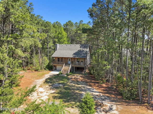 121 Pinewood Acres Dr, Powells Point, NC 27966 - rustic home featuring a porch, a wooded view, an attached garage, stairway, and dirt driveway