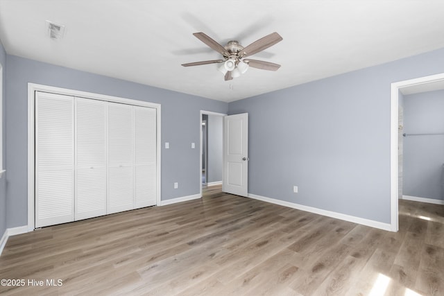 unfurnished bedroom featuring a ceiling fan, visible vents, wood finished floors, baseboards, and a closet