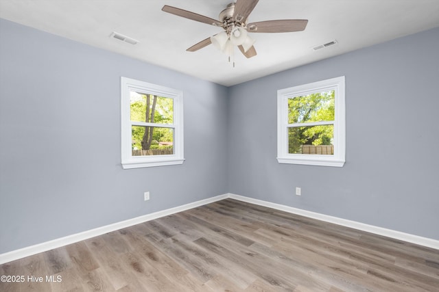 unfurnished room featuring visible vents, baseboards, wood finished floors, and a wealth of natural light