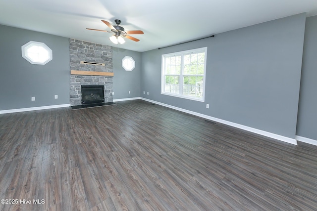 unfurnished living room with a ceiling fan, baseboards, dark wood-type flooring, and a stone fireplace