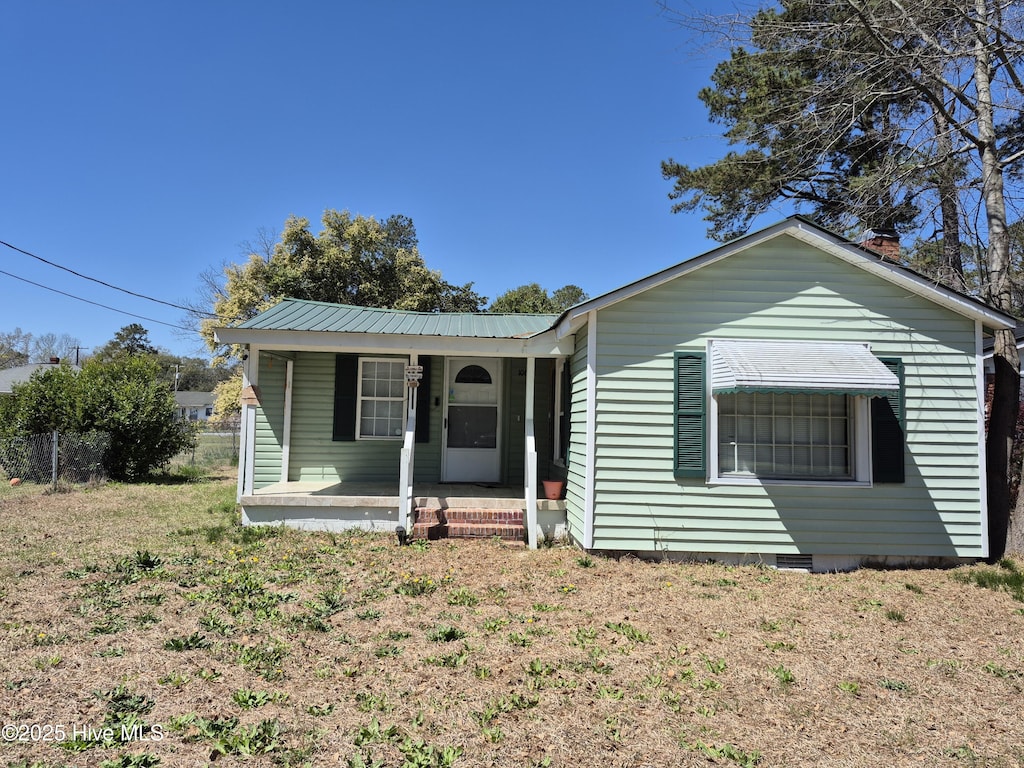 view of front of house featuring a porch, fence, metal roof, and a front yard