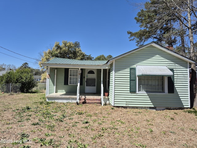view of front of house featuring a porch, fence, metal roof, and a front yard
