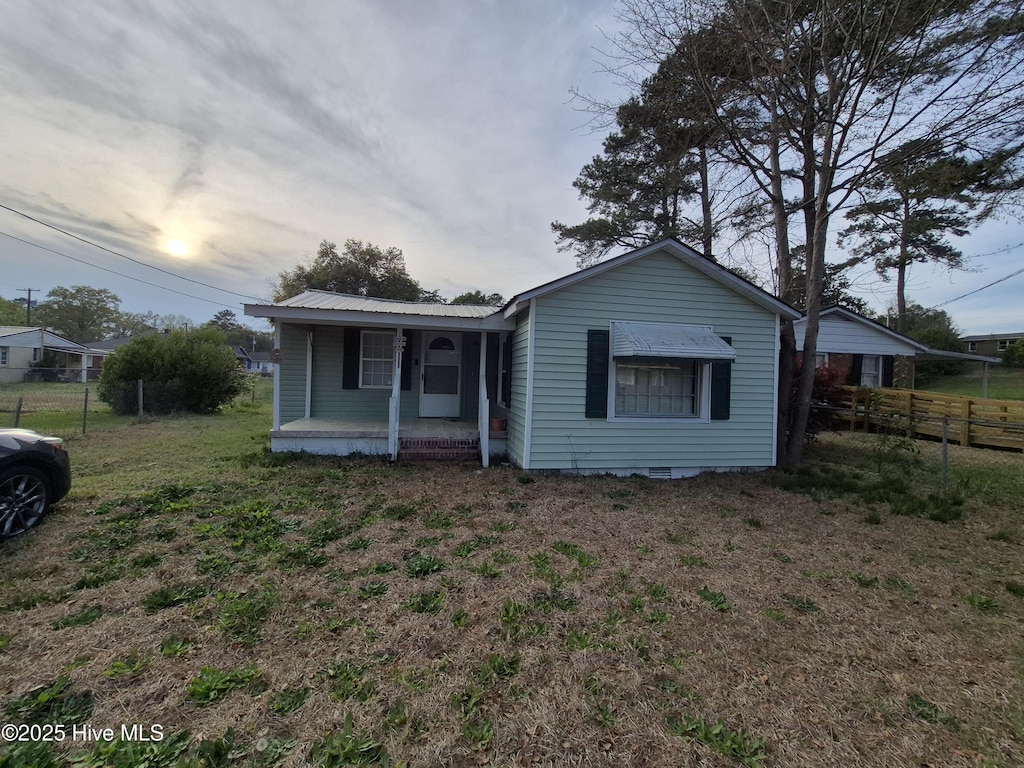 view of front facade featuring a front lawn, metal roof, covered porch, and fence