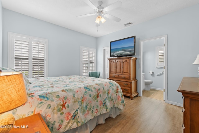 bedroom with visible vents, baseboards, light wood finished floors, a ceiling fan, and ensuite bath