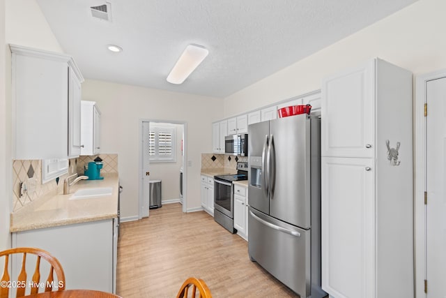 kitchen with decorative backsplash, appliances with stainless steel finishes, white cabinets, a sink, and visible vents
