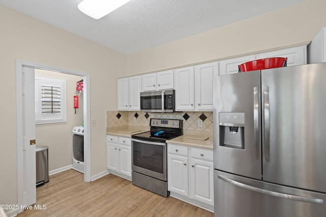 kitchen featuring decorative backsplash, stainless steel appliances, washer / dryer, light wood-type flooring, and light countertops
