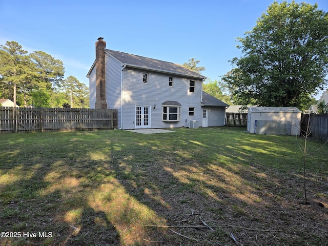 back of house with a chimney, a fenced backyard, french doors, a lawn, and a storage unit