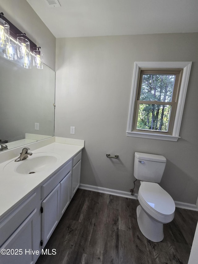 half bathroom with wood finished floors, vanity, toilet, and baseboards