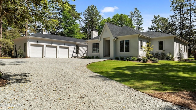 view of front of property featuring a chimney, gravel driveway, an outdoor structure, a front lawn, and an attached garage