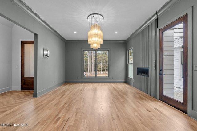 unfurnished dining area with an inviting chandelier, baseboards, crown molding, and light wood finished floors