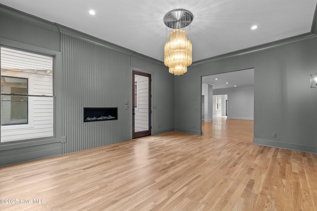 spare room featuring crown molding, an inviting chandelier, a large fireplace, baseboards, and wood finished floors