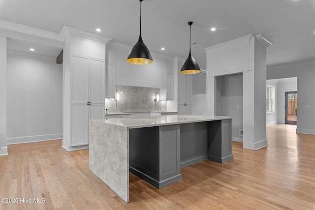 kitchen with decorative backsplash, ornamental molding, a large island, white cabinets, and light wood finished floors