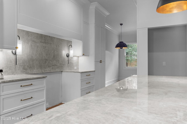 kitchen featuring crown molding, white cabinets, tasteful backsplash, light stone counters, and hanging light fixtures