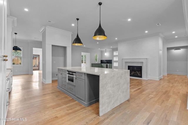 kitchen with crown molding, light wood-style floors, a center island, light stone counters, and gray cabinetry