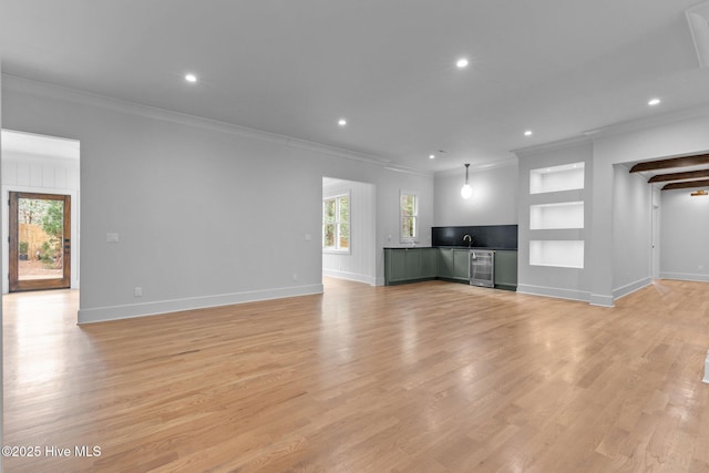 unfurnished living room featuring crown molding, built in features, baseboards, wine cooler, and recessed lighting