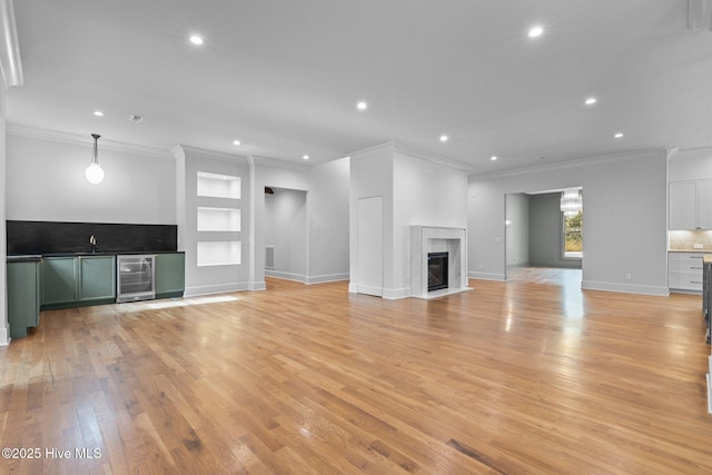unfurnished living room with light wood-type flooring, built in shelves, beverage cooler, ornamental molding, and recessed lighting