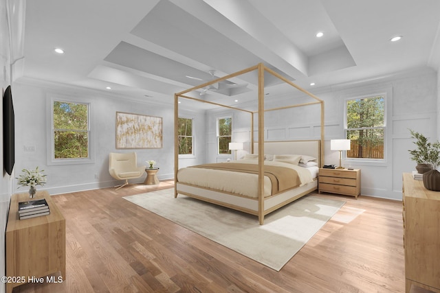 bedroom with a tray ceiling, multiple windows, and light wood finished floors