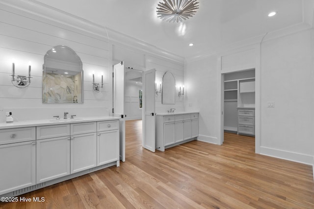 full bathroom featuring baseboards, ornamental molding, wood finished floors, and two vanities