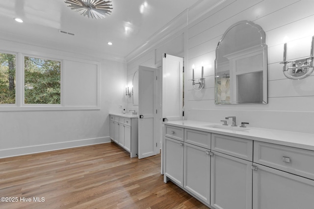 bathroom with a sink, crown molding, wood finished floors, and two vanities