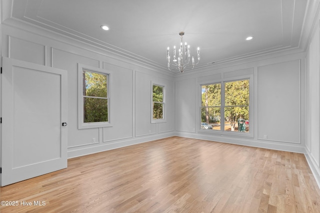 spare room featuring crown molding, a decorative wall, a notable chandelier, and a wealth of natural light