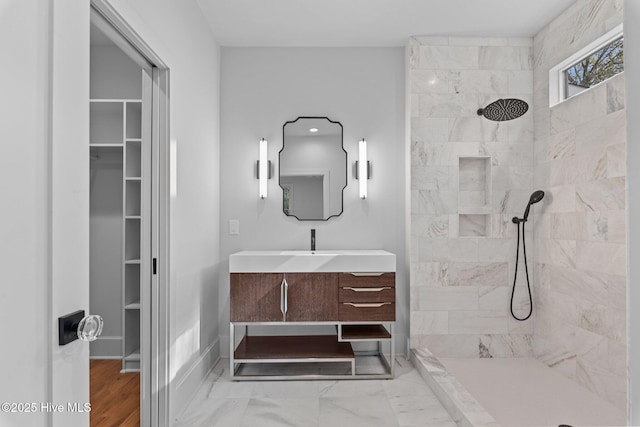 bathroom featuring a walk in closet, a tile shower, vanity, baseboards, and marble finish floor