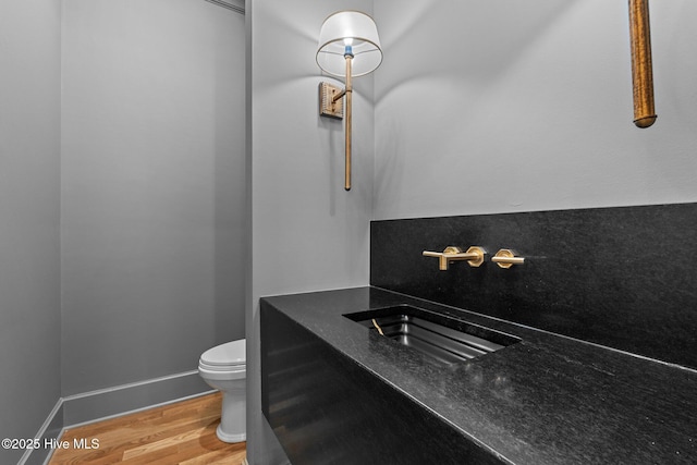 half bath with a sink, baseboards, toilet, and wood finished floors
