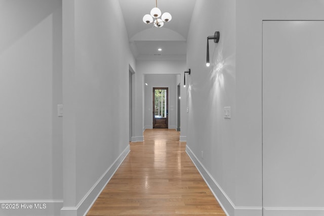 hall featuring baseboards, lofted ceiling, an inviting chandelier, and light wood finished floors