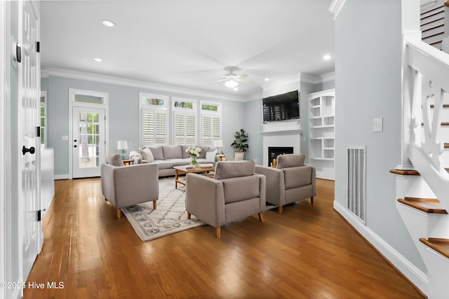 living room with stairway, ceiling fan, wood finished floors, and ornamental molding