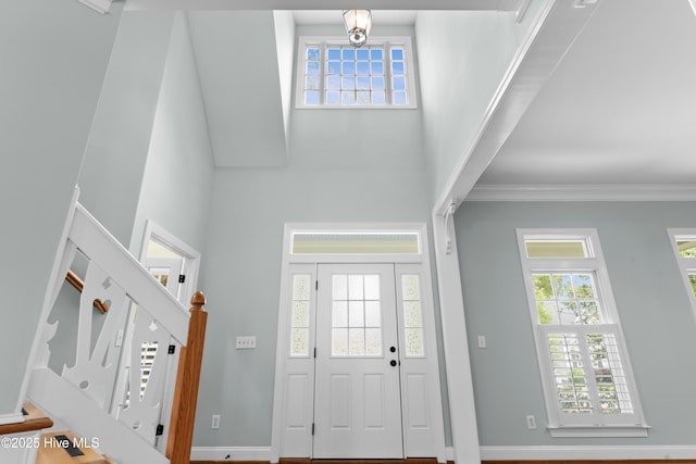 entrance foyer with ornamental molding, a towering ceiling, stairway, and baseboards