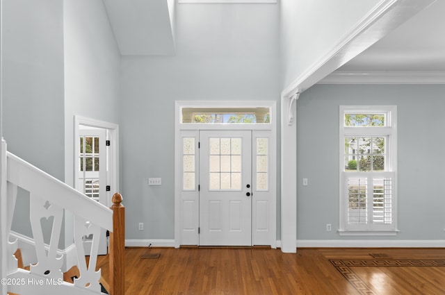 entryway with ornamental molding, a high ceiling, wood finished floors, and baseboards