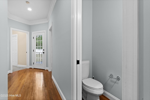 bathroom featuring baseboards, wood finished floors, toilet, and crown molding