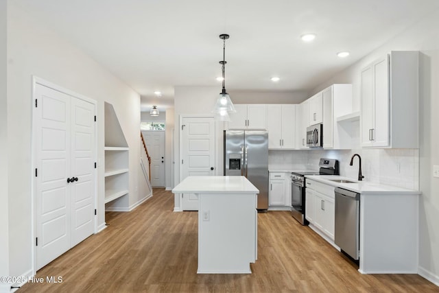 kitchen featuring stainless steel appliances, light wood-style floors, a kitchen island, backsplash, and a sink