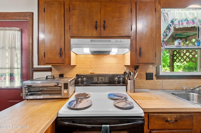 kitchen with a sink, a toaster, under cabinet range hood, light countertops, and electric stove