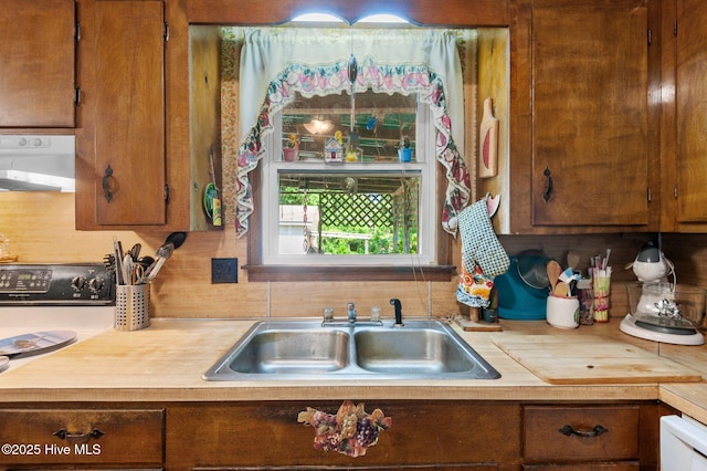 kitchen featuring light countertops, brown cabinetry, a sink, and extractor fan