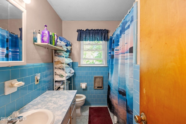 bathroom with tile walls, toilet, tile patterned floors, vanity, and a wainscoted wall
