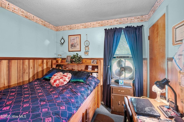bedroom featuring a textured ceiling, carpet, and a wainscoted wall